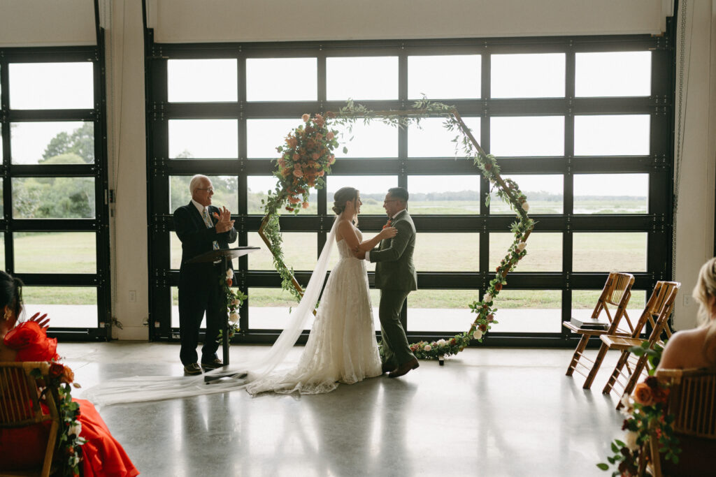 indoor wedding ceremony at lakeside wedding venue with bride and grooms and officiant.