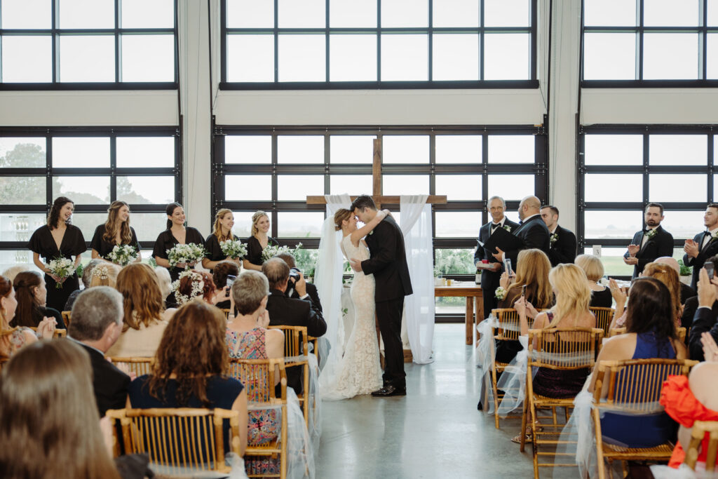 bride and groom sharing first kiss as married couple, central florida wedding barn venue, luxury barn wedding venue in Florida with bridesmaids and groomsmen