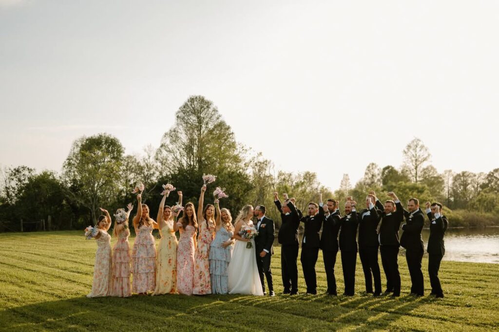 bridal party post ceremony celebrating while bride and groom kiss at luxury barn wedding venue