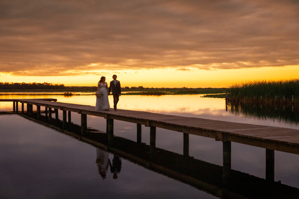 bride and groom walking hand in hand at sunset on Lake Toho at Orlando Wedding venue