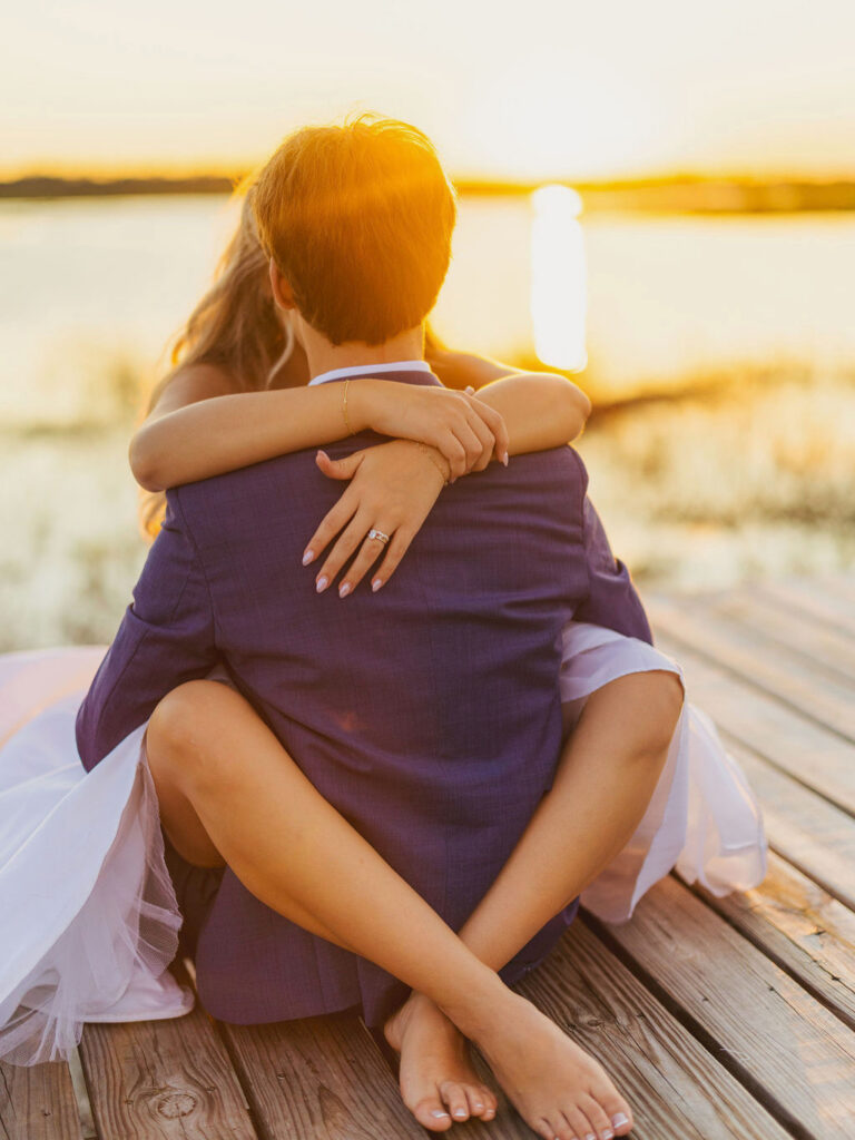 bride and groom sitting on the dock for sunset photos after their wedding during the creative session