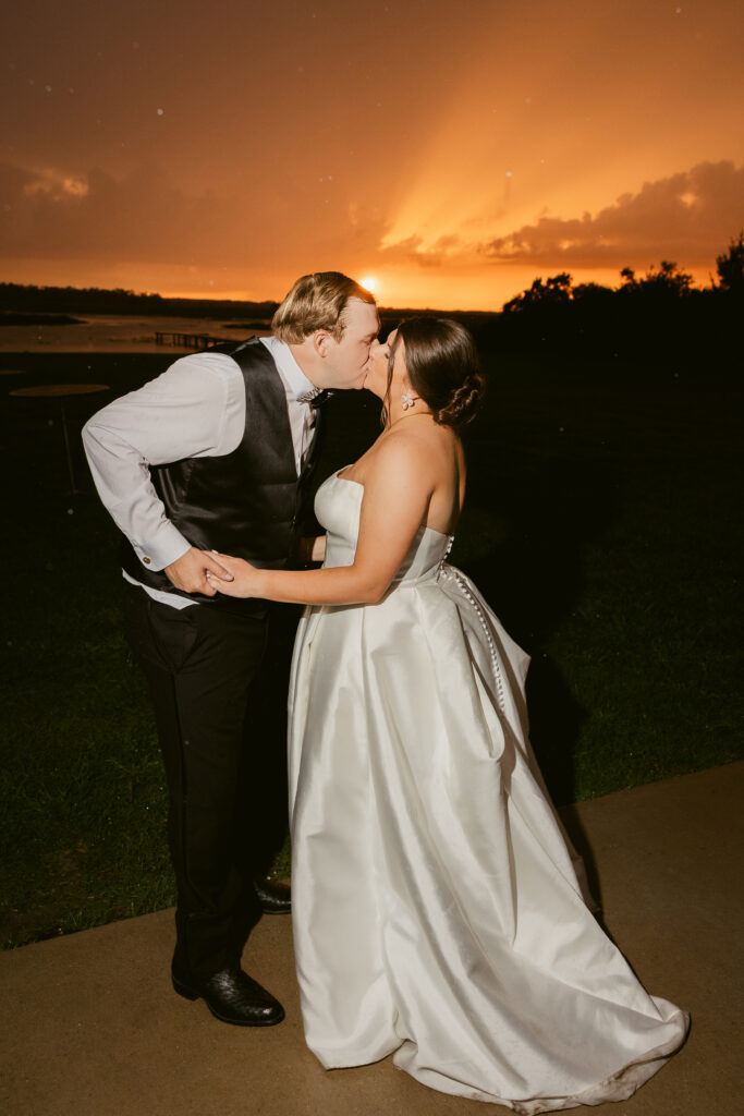 Bride and groom sharing a kiss at sunset on the lakeside wedding venue
 