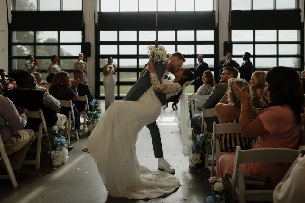 bride and groom in a dip kiss in the aisle at indoor wedding ceremony