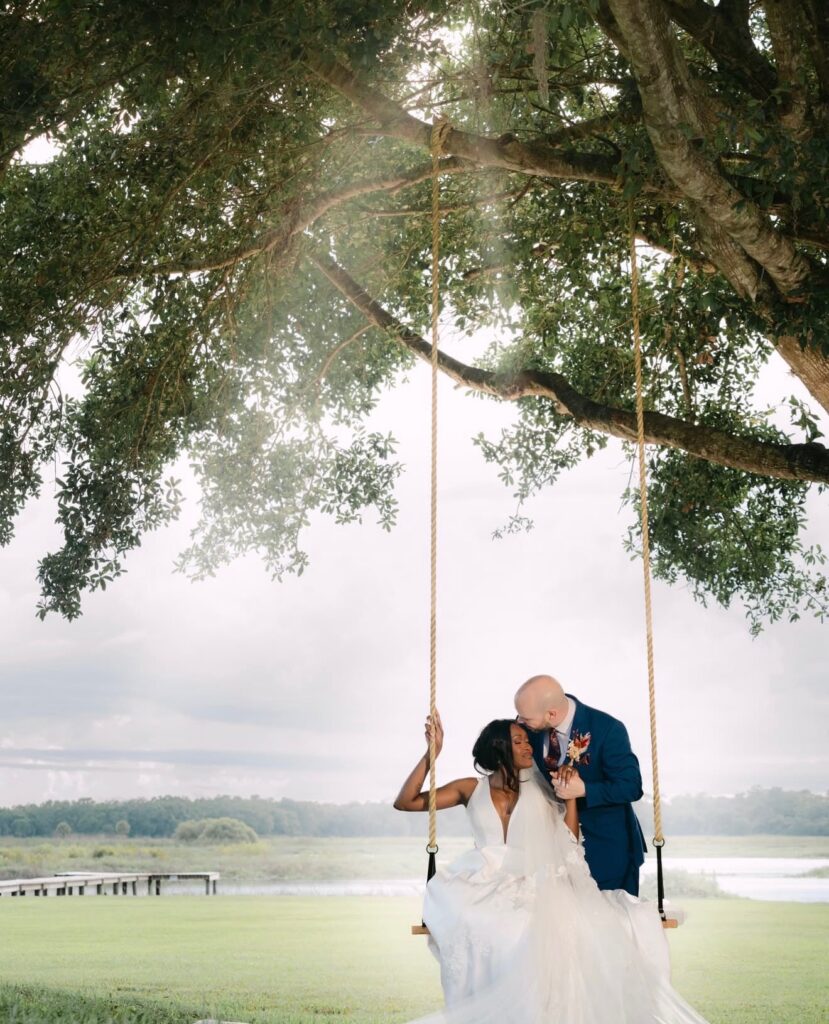bride and groom sitting on swing hanging from the tree at lakeside wedding venue in Central Florida