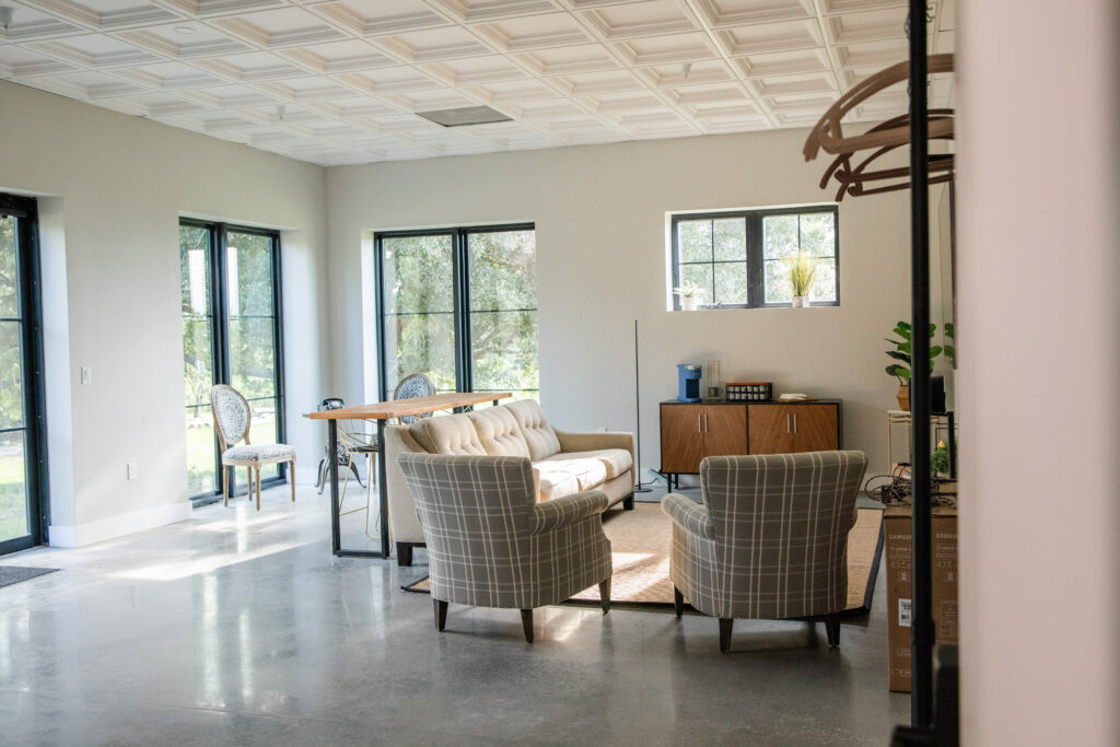 Spacious getting ready room with bars to hang clothes, chairs, with a seating area and bar behind the couch.