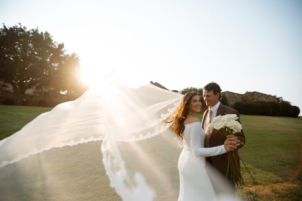 bride holding her bouquet with groom while the wind catches her veil in the sunlight, Florida wedding